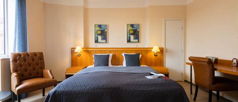 A hotel room with a large bed, two side chairs, a wooden nightstand, and two wall-mounted lamps.
