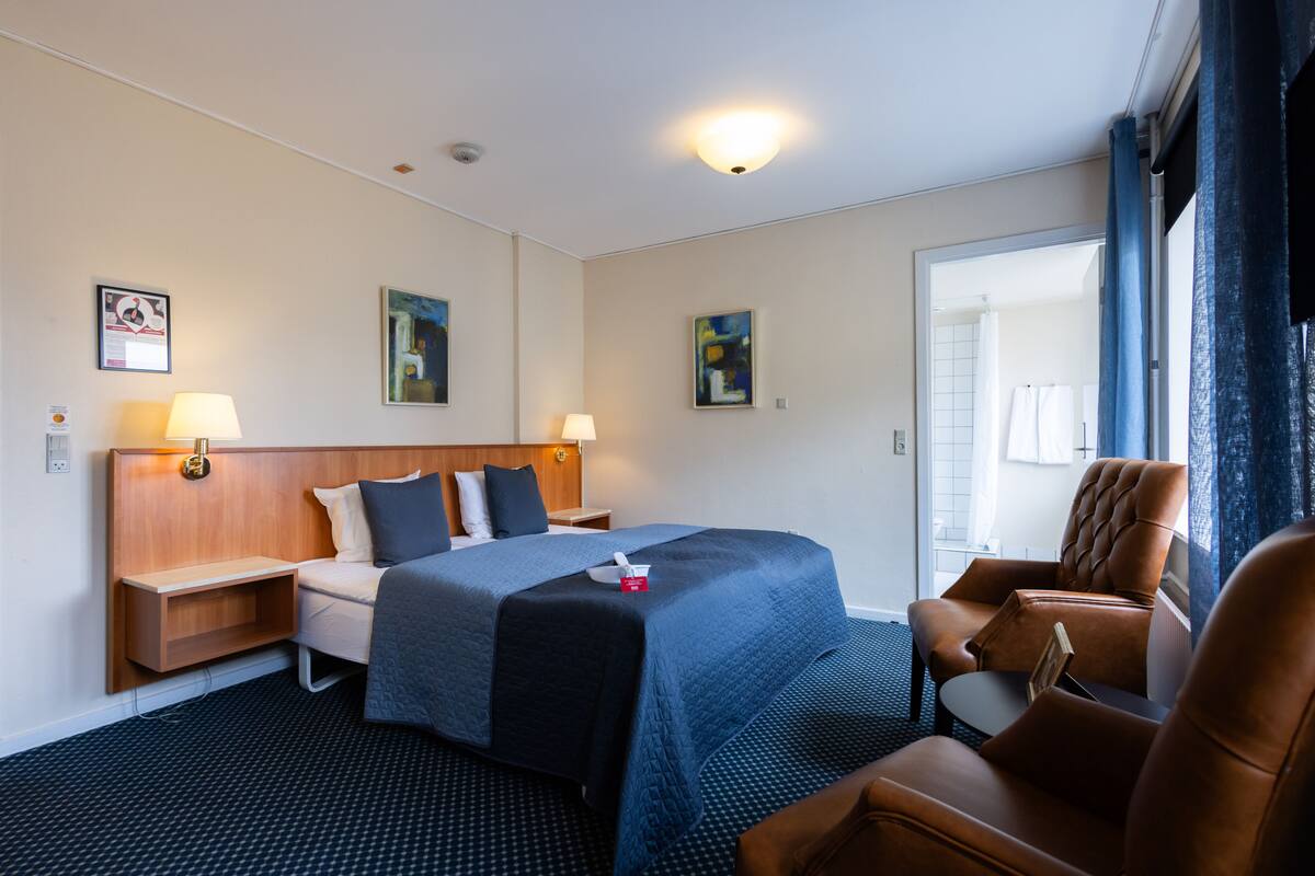 A hotel room with a bed, two bedside tables, a chair, and artwork on the walls.