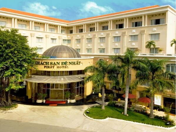 Experience the elegant Khách Sạn Định First Hotel's symmetrical facade with a central dome structure and beautifully landscaped surroundings.