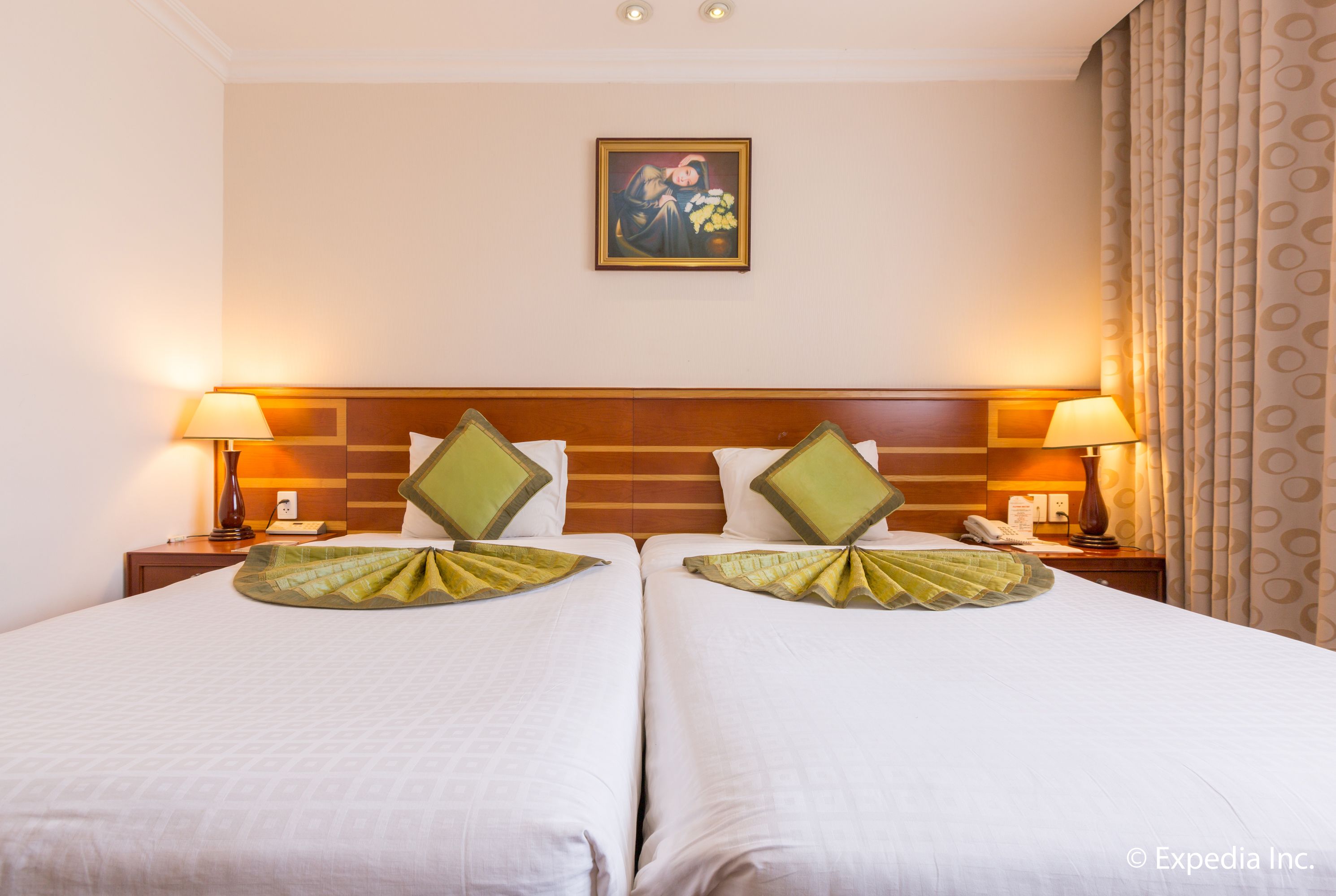 A hotel room with two beds, a wooden headboard, bedside lamps, and a painting on the wall.