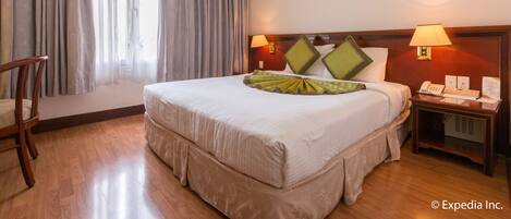 Ein Hotelzimmer mit einem großen Bett, zwei Nachttischlampen, einem Nachttisch, einem Sessel und einem Fenster mit Vorhängen.