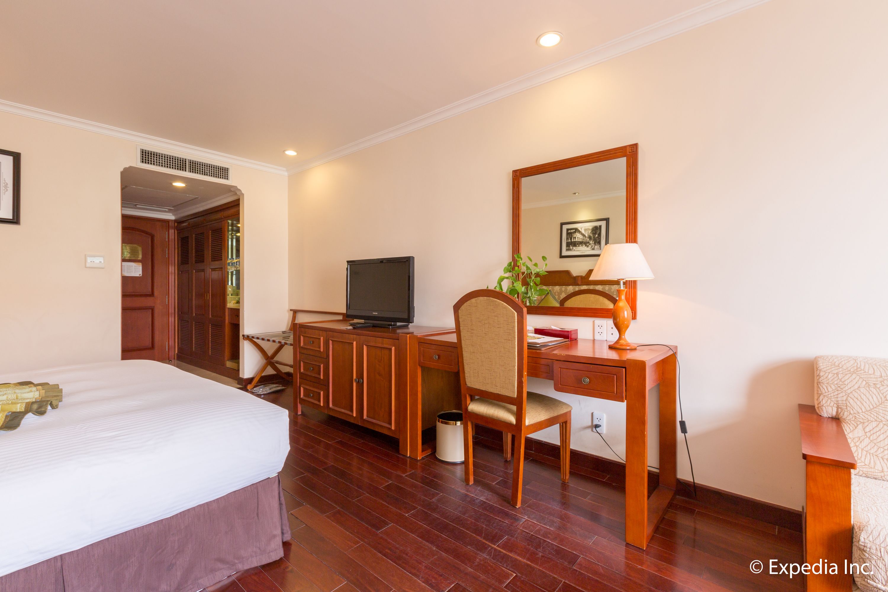 Una habitación de hotel con una cama, un escritorio con computadora, televisión y espejo.