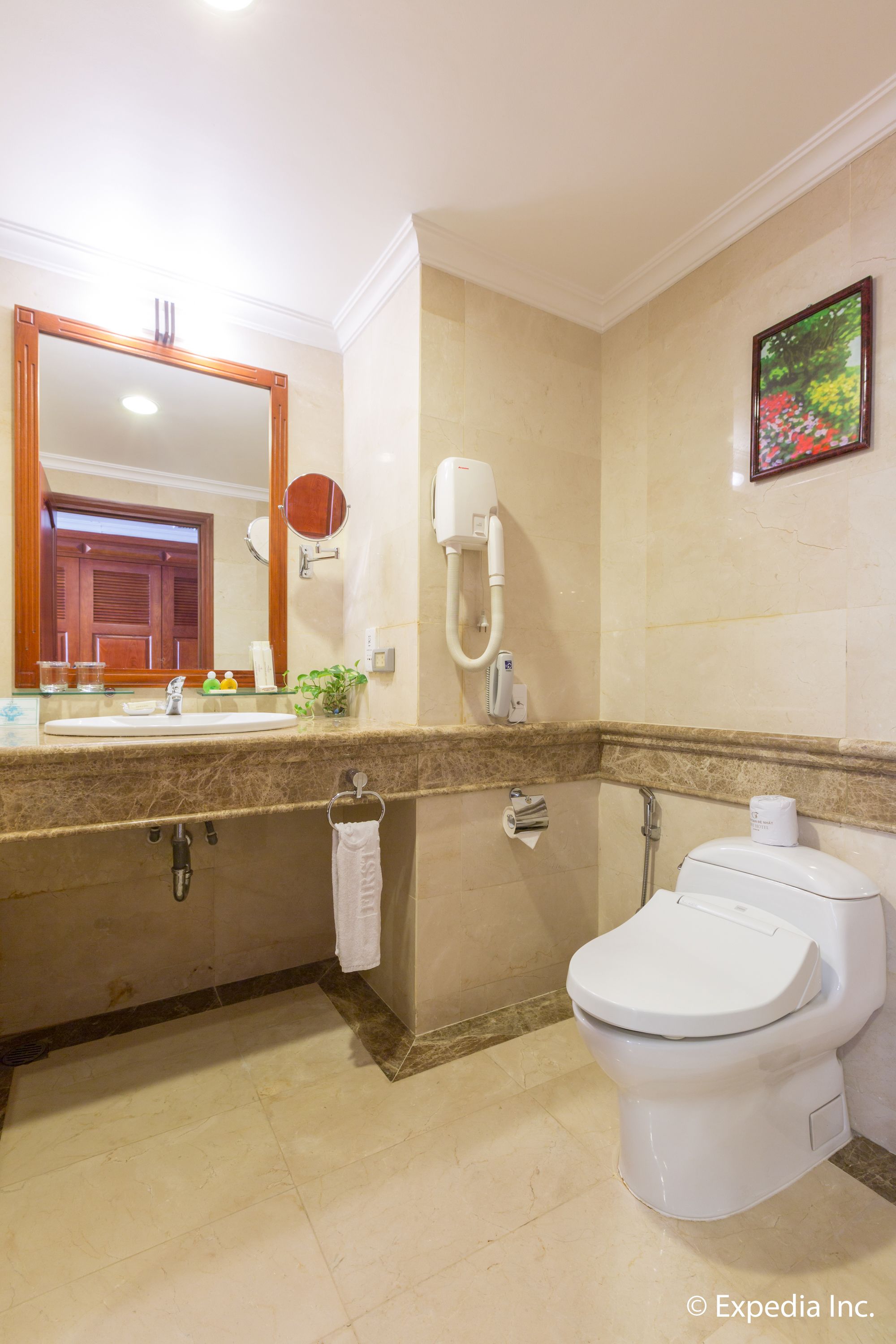 Un baño con lavamanos de mármol, inodoro, secamanos y espejo.