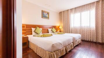 Habitación de hotel con dos camas, cabecero de madera, cortinas estampadas y un cuadro en la pared.