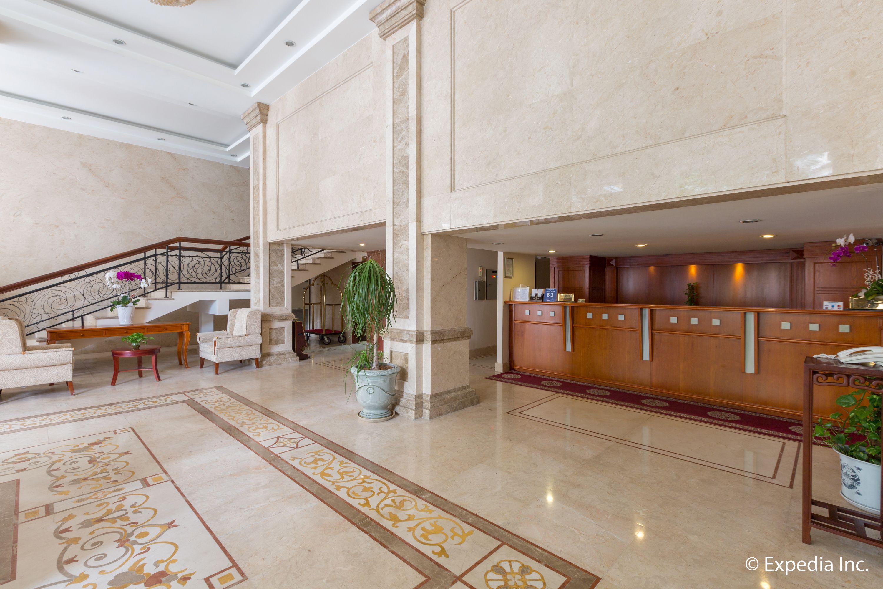 A spacious lobby with a marble floor, a reception desk, seating area, and a staircase.
