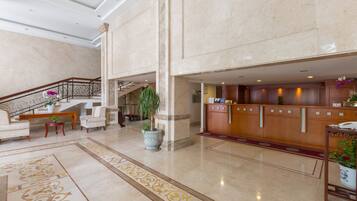 A spacious lobby with a marble floor, a reception desk, seating area, and a staircase.