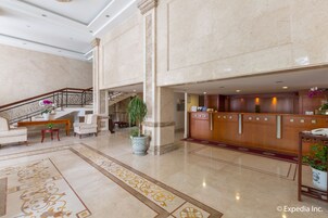 A spacious lobby with a marble floor, a reception desk, seating area, and a staircase.