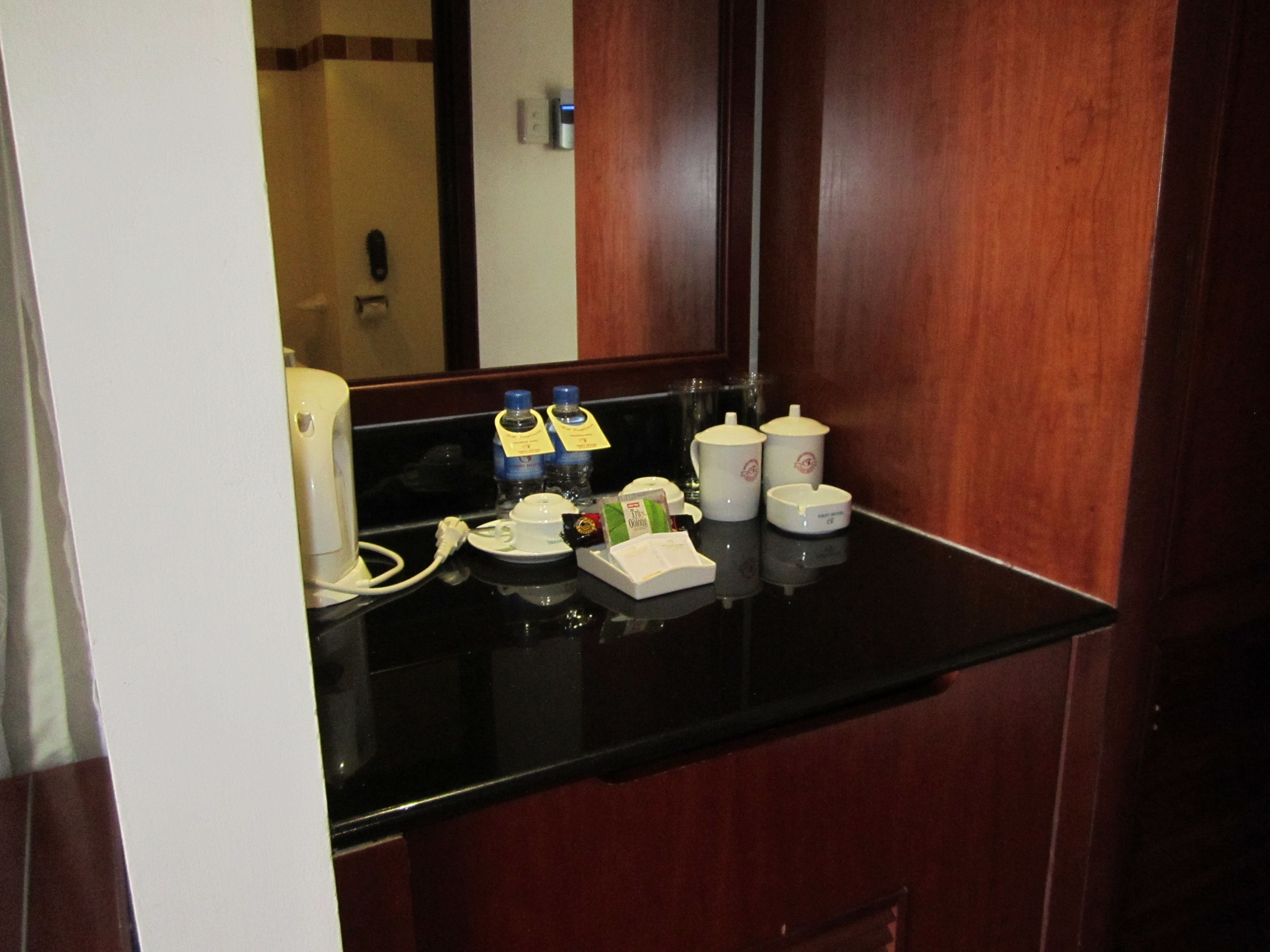 A hotel room's coffee station with a coffee maker, two bottles of water, a tea set, and a small box of tissues.