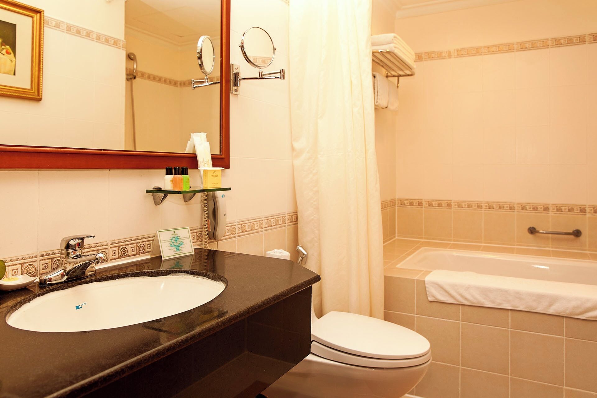 A bathroom with a sink, toilet, and bathtub. There are toiletries on the sink, a towel rack, and a shower curtain.