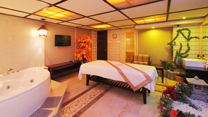 A hotel room with a large bathtub, a bed with a white bedspread, a television on the wall, and a small table with a plant. - First Hotel (Ho Chi Minh City)