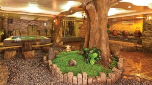 A pool table, a large tree, and a stone wall in a room with a wooden floor and stone walls. - First Hotel (Ho Chi Minh City)
