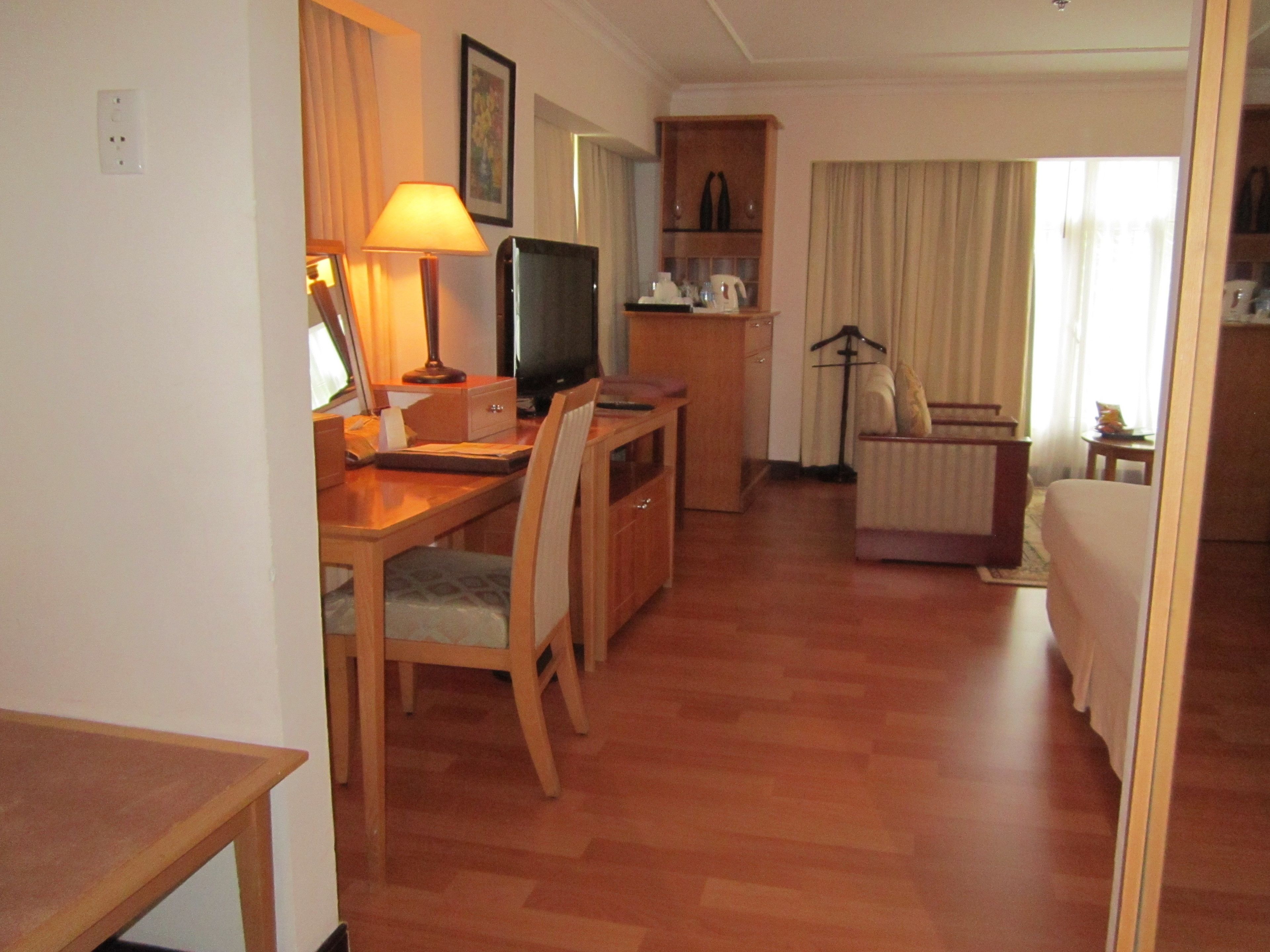 Hotellihuone, jossa on puinen työpöytä, televisio, tuoli, sohva ja pieni pöytä, jossa on lamppu.
