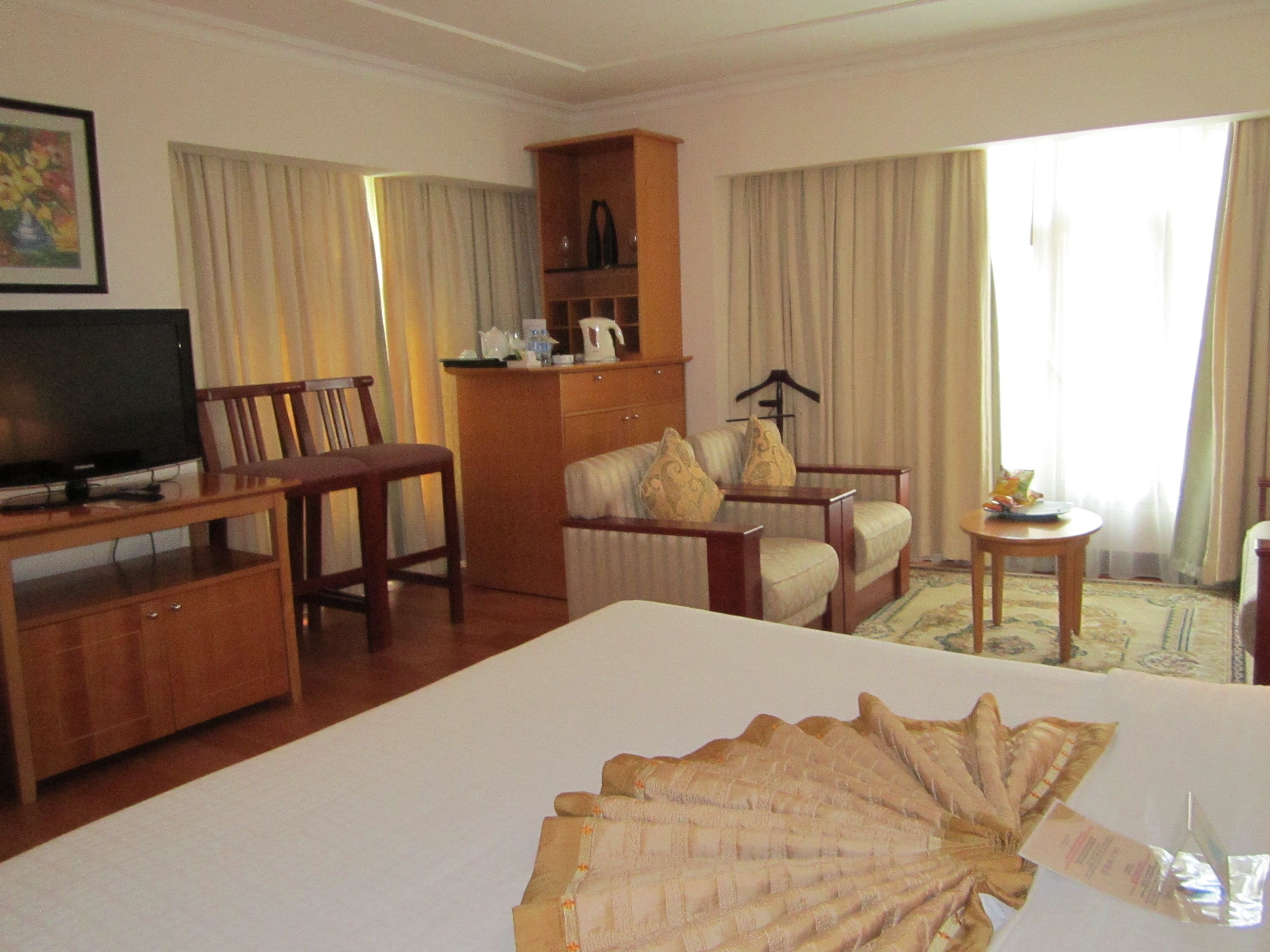Une chambre d’hôtel avec un grand lit, une télévision, un bureau en bois, une chaise, un canapé, une petite table et une armoire.