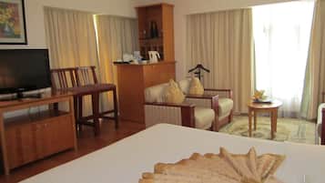A hotel room with a large bed, a TV, a wooden desk, a chair, a sofa, a small table, and a wardrobe.