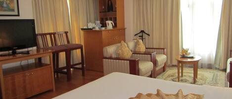 Une chambre d’hôtel avec un grand lit, une télévision, un bureau en bois, une chaise, un canapé, une petite table et une armoire.