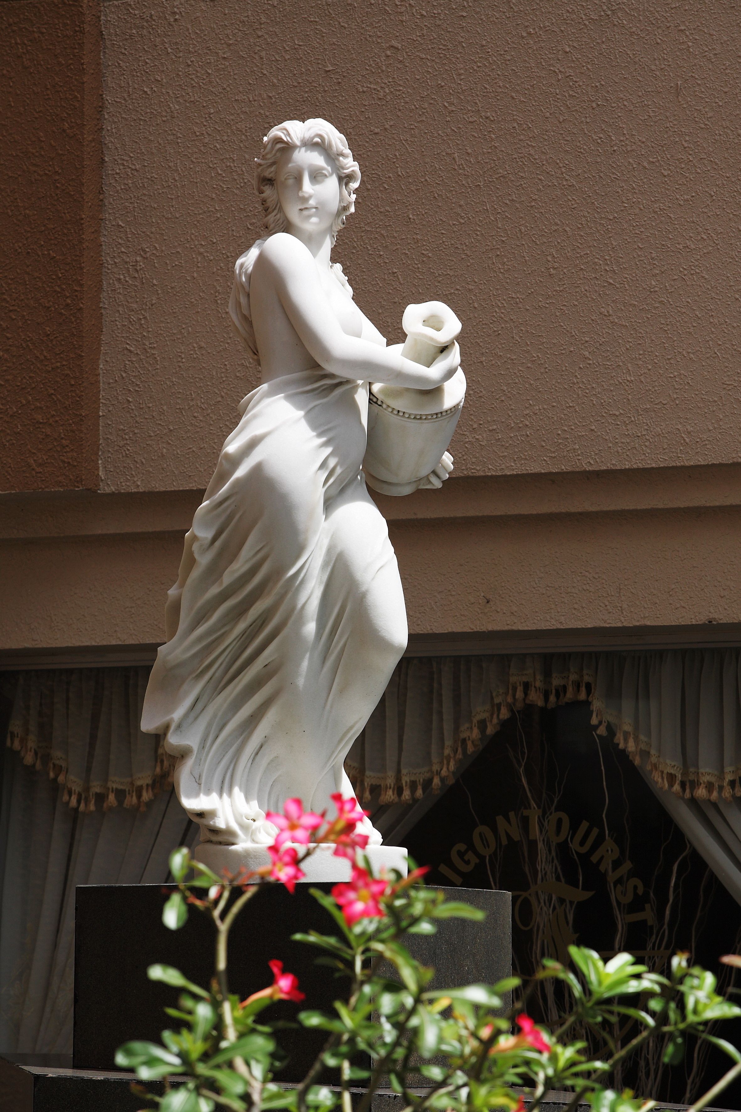 Una estatua de una mujer sosteniendo una cesta, ubicada frente a un edificio con un letrero que dice 'LIGONTOURIST'.