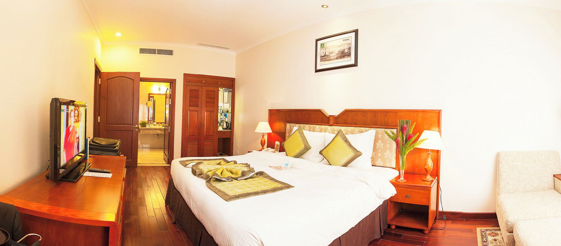 A hotel room with a bed, bedside tables, a TV, a desk, and a chair.