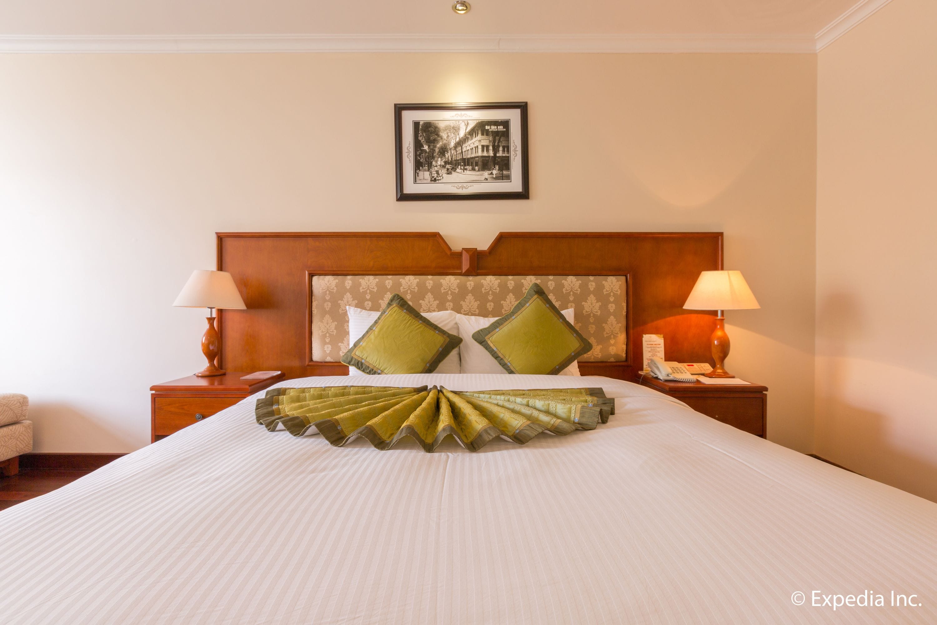 Quarto de hotel com uma cama grande, duas mesas de cabeceira com luminárias, cabeceira com almofadas decorativas e um quadro na parede.