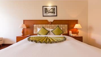 Quarto de hotel com uma cama grande, duas mesas de cabeceira com luminárias, cabeceira com almofadas decorativas e um quadro na parede.
