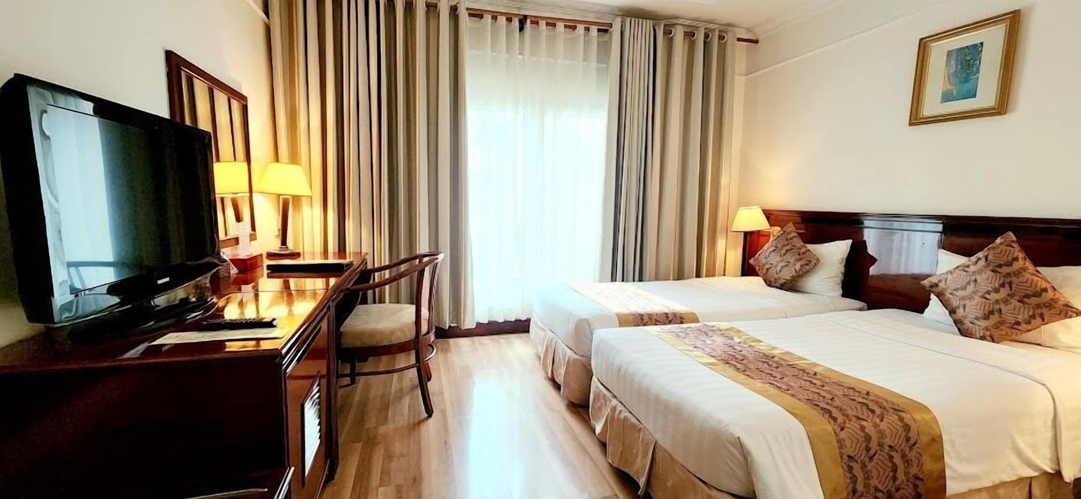 A hotel room with two beds, a desk with a television, and a chair.