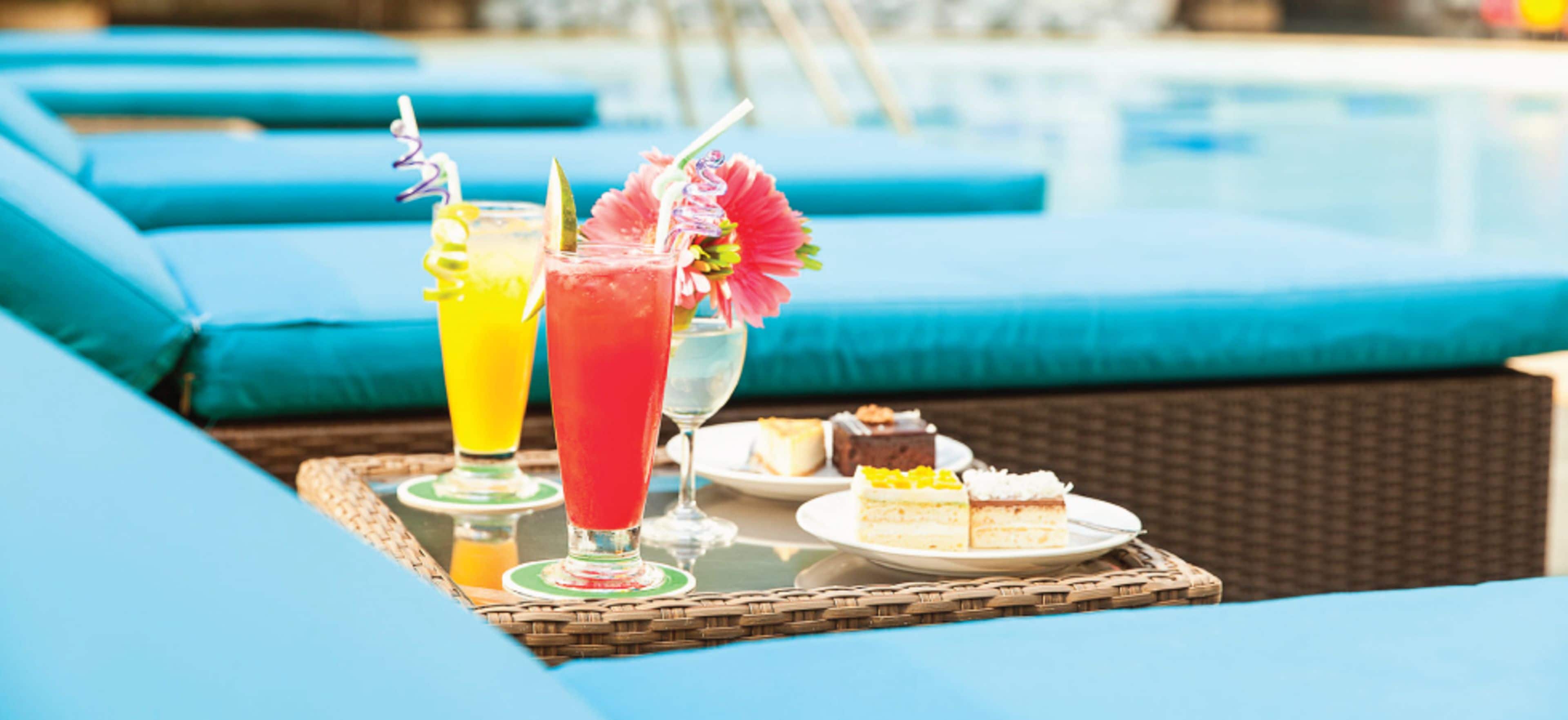 Un espace aménagé au bord de la piscine, avec des chaises longues, une table où sont servis des boissons et une part de gâteau.