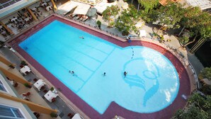 A large indoor swimming pool with a red border, surrounded by lounge chairs and umbrellas. - First Hotel (Ho Chi Minh City)