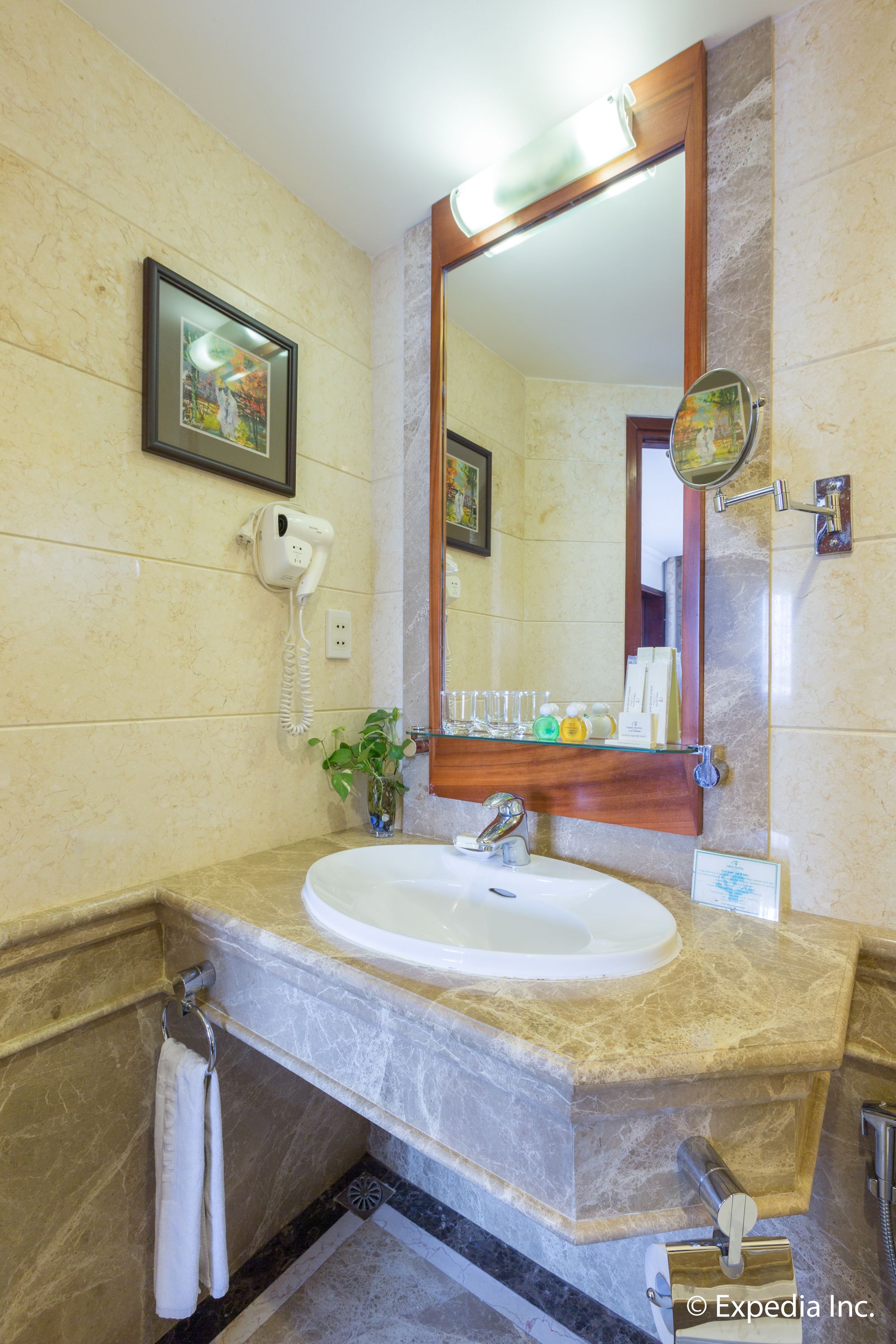 Un baño con lavamanos de mármol, un cuadro enmarcado, un secador de pelo y un espejo.