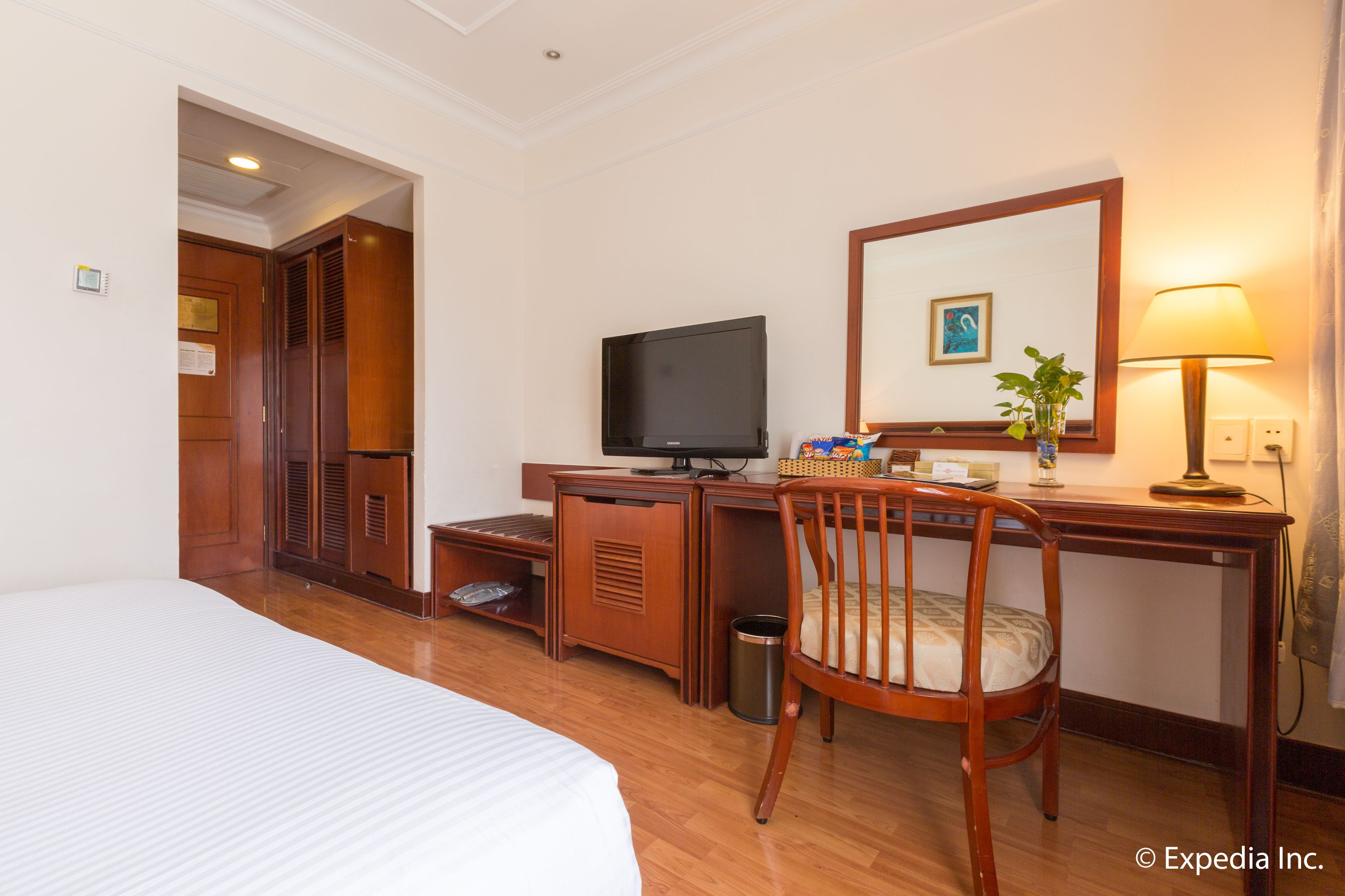 A hotel room with a bed, desk, television, chair, and a small trash can.