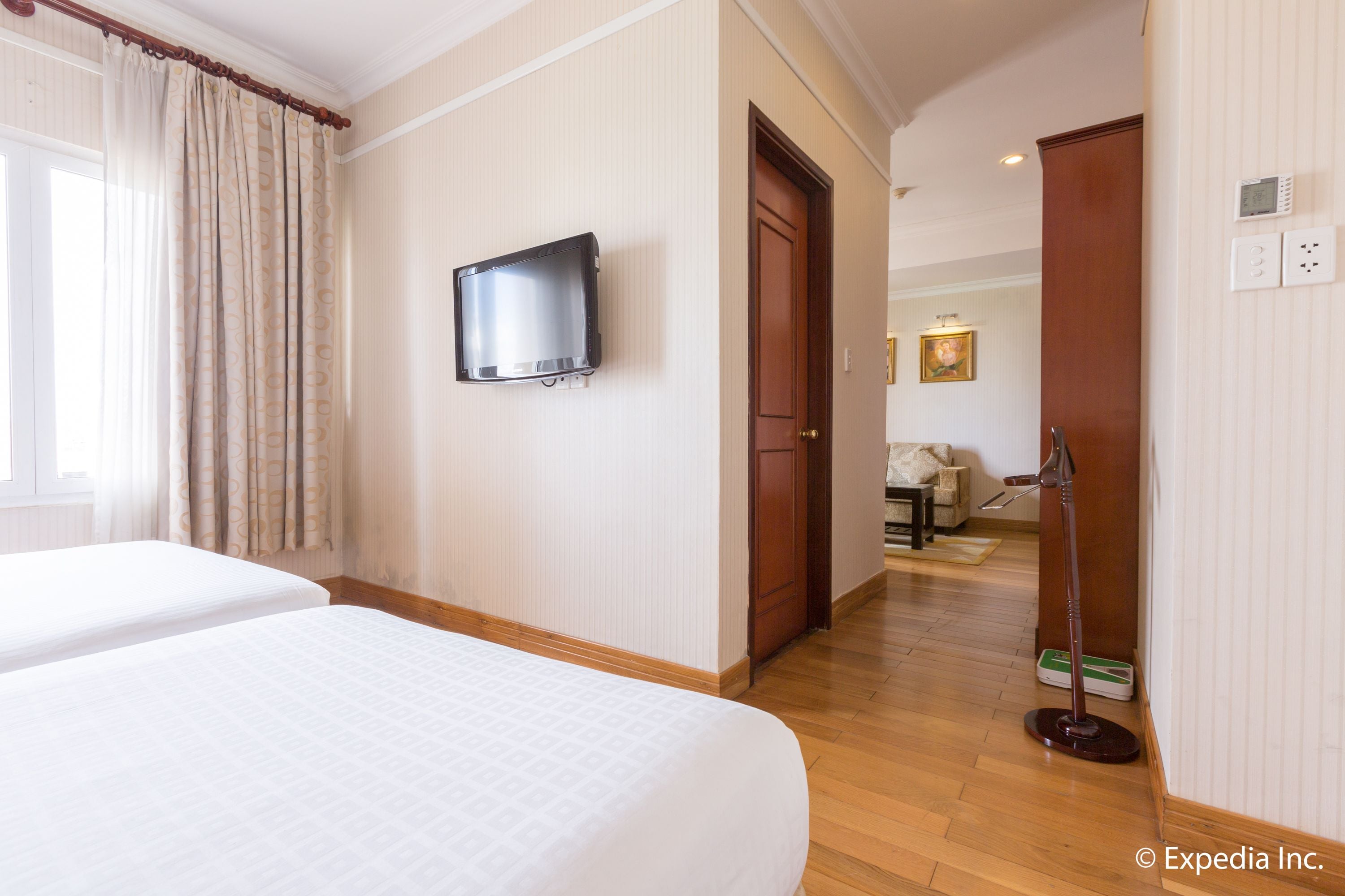 A hotel room with two beds, a television, a wooden floor, and a door leading to another room.
