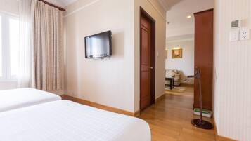 A hotel room with two beds, a television, a wooden floor, and a door leading to another room.