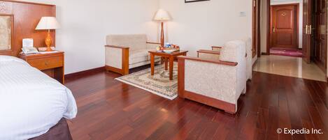 A hotel room with a bed, two armchairs, a small table, a lamp, a telephone, and a framed picture on the wall.