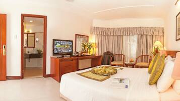 Habitación de hotel con cama, escritorio, televisión y baño visible a través de una puerta abierta.