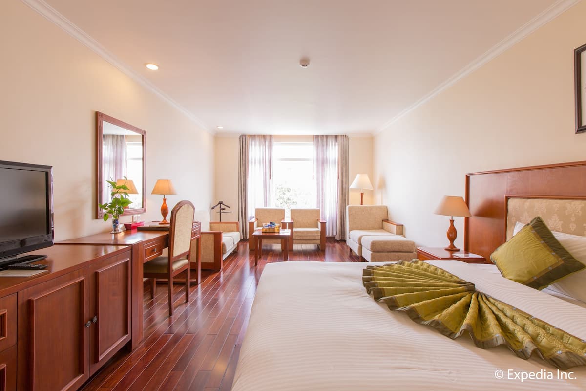 Habitación de hotel con una cama grande, un escritorio con televisor, dos sillones, un sofá y una ventana con cortinas.