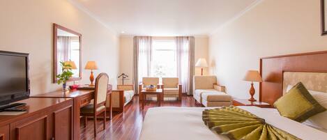 A hotel room with a large bed, a desk with a television, two armchairs, a sofa, and a window with curtains.
