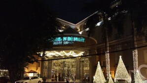 A hotel with a prominent sign, large windows, and Christmas trees. - First Hotel (Ho Chi Minh City)