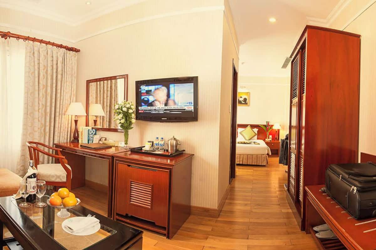 Habitación de hotel con un conjunto de sofá, una mesa de centro, un escritorio con lámpara, televisión y una maleta en un banco.