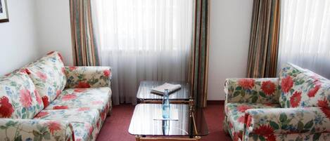 A room with two floral-patterned sofas, a glass-top coffee table, and striped curtains.