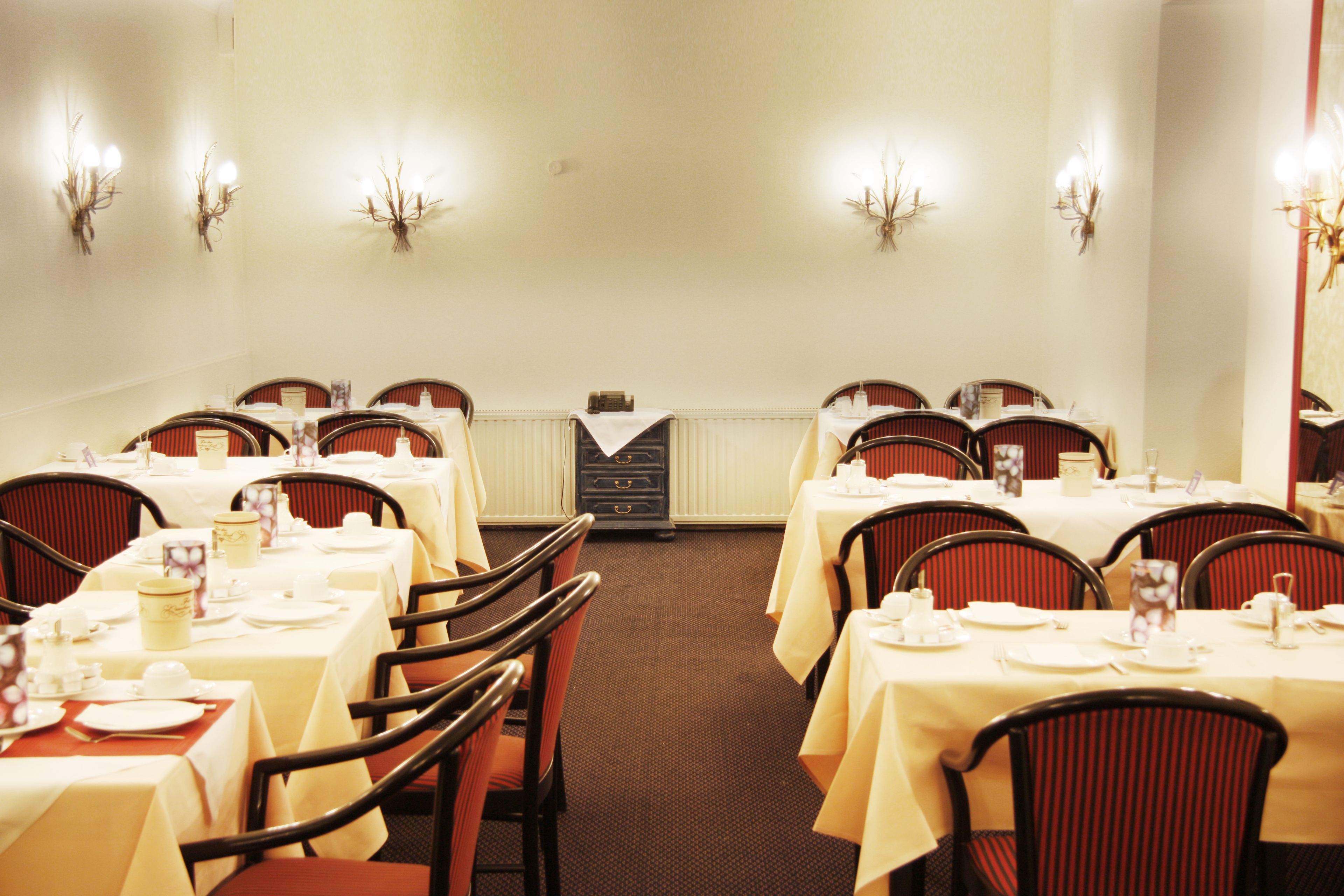 Un comedor con varias mesas y sillas, cada conjunto con manteles blancos y cubiertos.