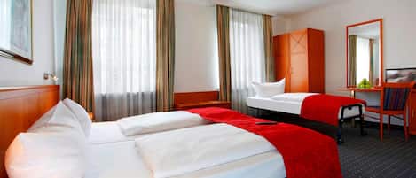 A hotel room with a large bed, a desk, a chair, and a wardrobe.