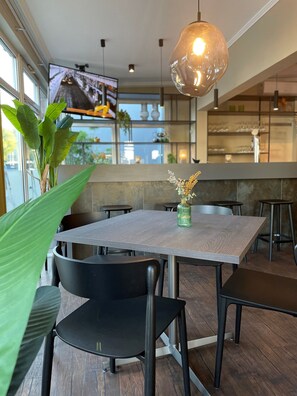 A modern dining area with a wooden table, black chairs, a hanging light fixture, and a view of the city through large windows.