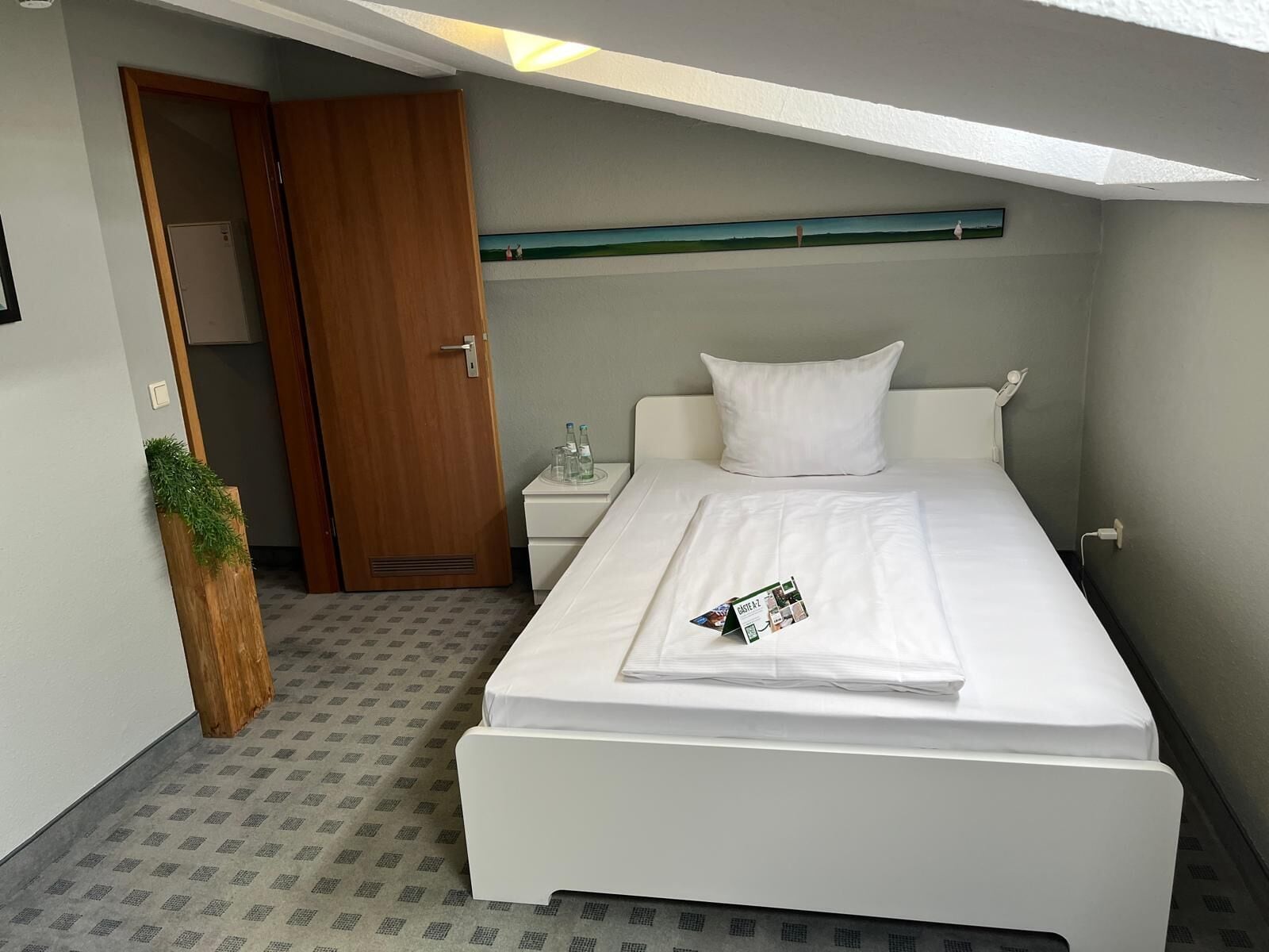 Ein Hotelzimmer mit Bett, Nachttisch, Tür und einer kleinen Pflanze.