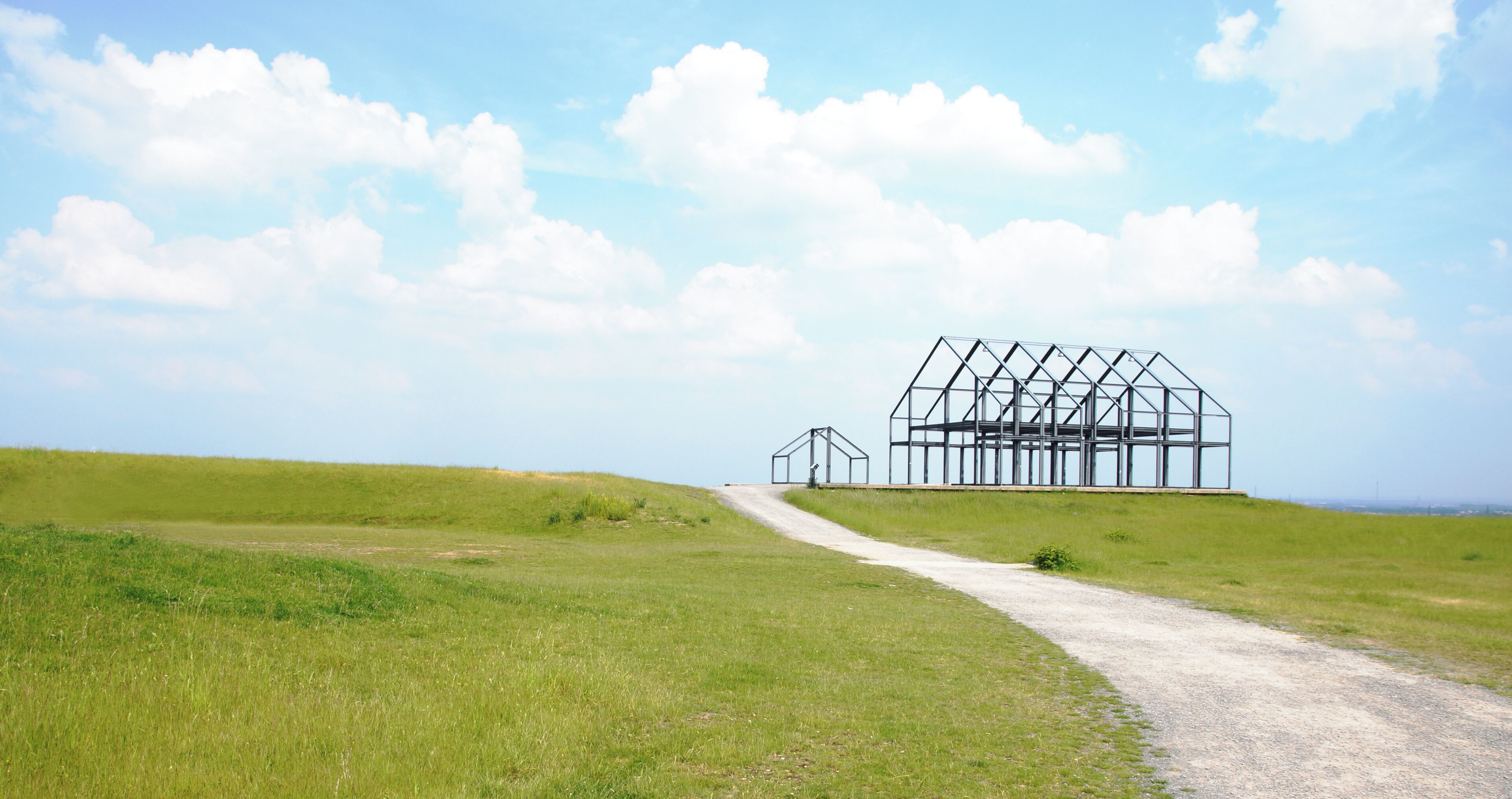 Een landelijk landschap met een onverharde weg die leidt naar een grote, onvoltooide metalen constructie.