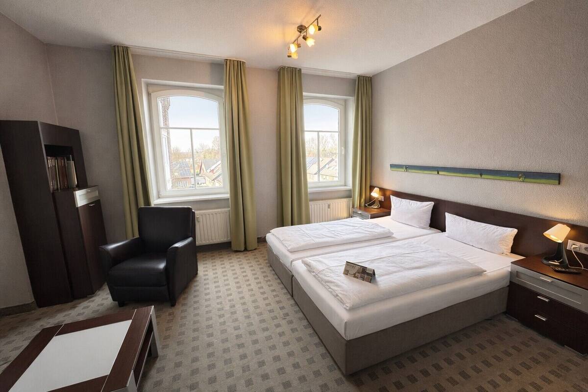 A hotel room with a bed, a chair, a desk, and a window with curtains.