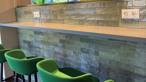 A modern kitchen with a green-tiled backsplash, bar stools, pendant lighting, and a view of the outdoors. - Hotel Dampfmühle (Neukirchen-Vluyn)