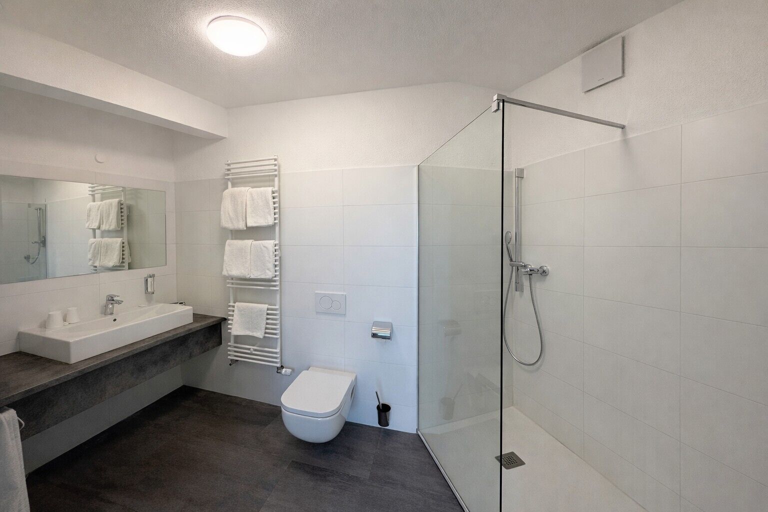 Un baño moderno con cabina de ducha de vidrio, un inodoro blanco, un lavabo con encimera de mármol y un toallero con varias toallas.