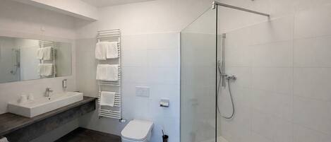 Un baño moderno con cabina de ducha de vidrio, un inodoro blanco, un lavabo con encimera de mármol y un toallero con varias toallas.