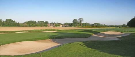 A golf course with sand bunkers, well-maintained grass, and a clear sky.