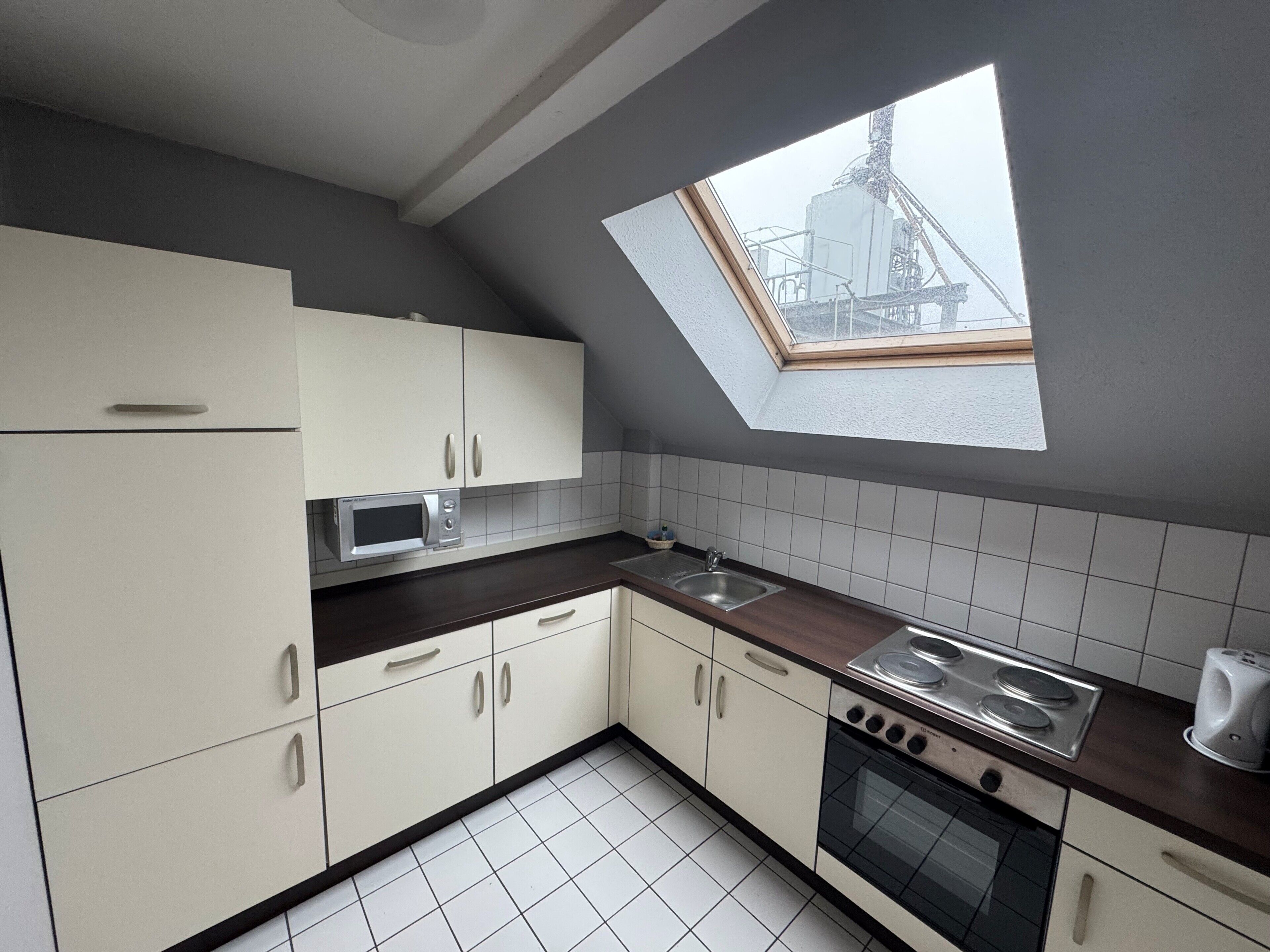 A kitchen with white cabinets, a microwave, a sink, a stove, and a skylight.