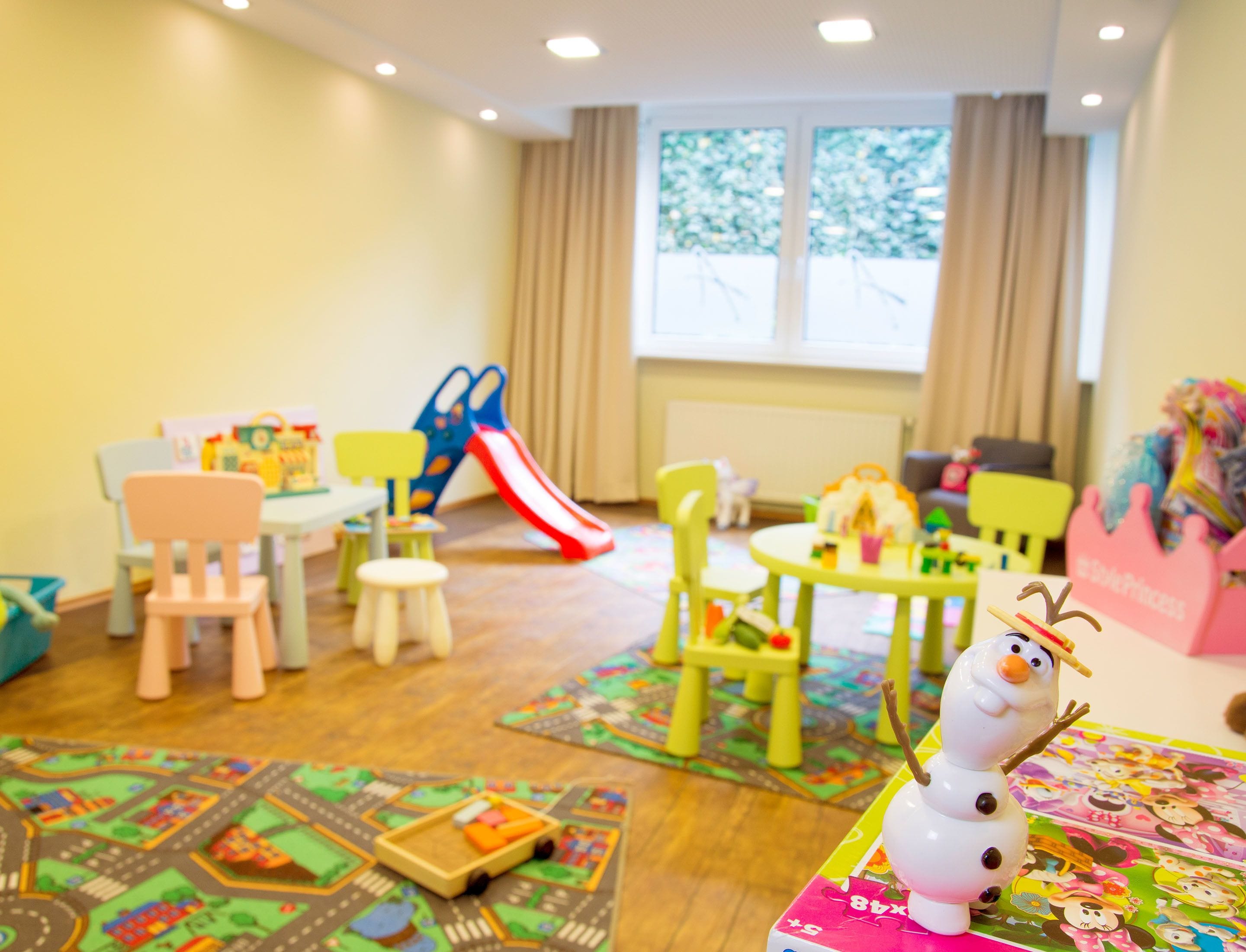Ein Spielzimmer für Kinder mit Rutsche, Stühlen, Tischen und Lernspielzeug.