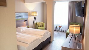 A hotel room with two beds, a desk with a lamp, a chair, a TV, and a window with curtains. - Hotel Dampfmühle (Neukirchen-Vluyn)